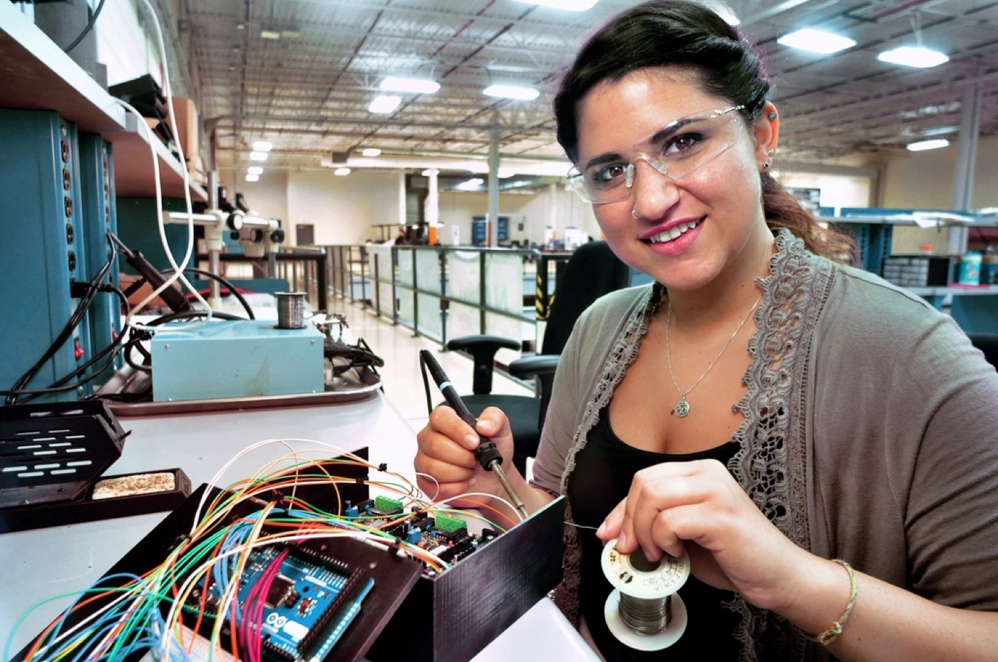 Engineer soldering wires on an electronics bench in a long workshop.