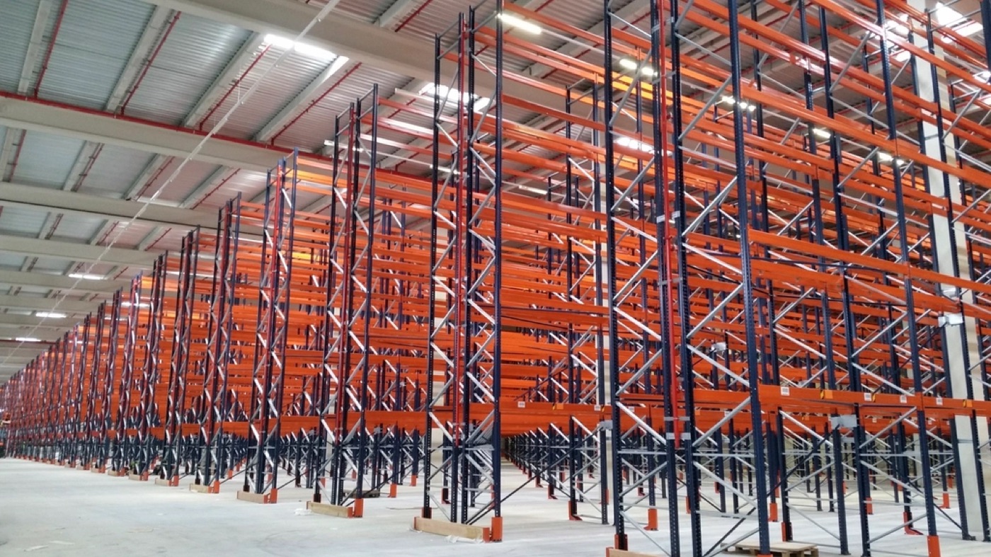 Long aisles of tall orange and blue pallet racking in an empty warehouse.