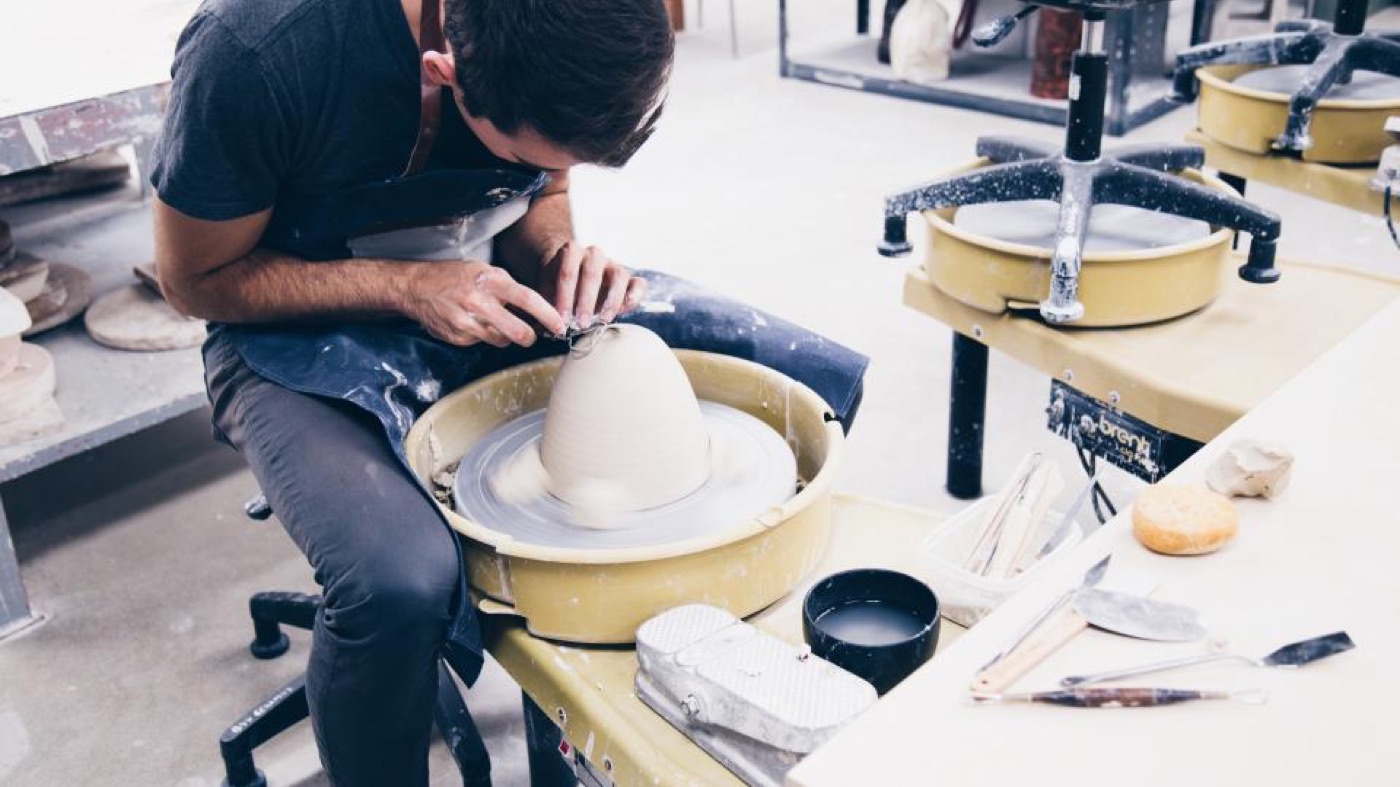 A potter shaping a clay vessel on a wheel, surrounded by tools.